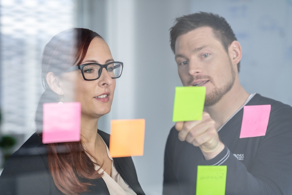 Zwei Mitarbeiter diskutieren über Post-Its.